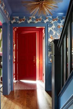 the hallway is painted bright blue and has red doors with floral wallpaper on it