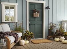 the front porch is decorated for fall with pumpkins and potted plants on the floor