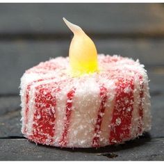 a small red and white cake sitting on top of a wooden table next to a yellow candle