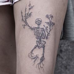 a skeleton tattoo on the thigh with flowers and branches growing out of it's back