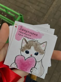 a hand holding three small cards with a cat on one and a heart on the other