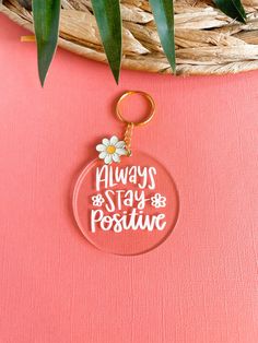 a keychain with the words always stay positive on it and daisies in white lettering