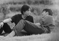 two young men sitting on the ground in a field