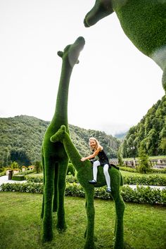 a woman sitting on top of a fake giraffe in the grass next to another fake giraffe