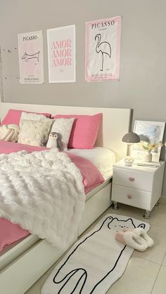 a white bed with pink sheets and pillows in a bedroom next to two pictures on the wall