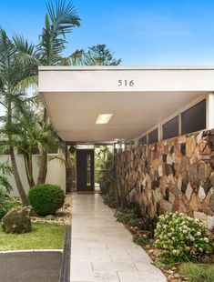 the entrance to a home with stone walls and palm trees in the front lawn area