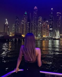 a woman is looking out over the water in front of a city skyline at night