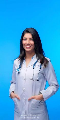 a woman wearing a white lab coat and holding her hands in the pockets while standing against a blue background