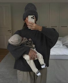 a woman taking a selfie while holding a baby in her arms and wearing a knitted hat