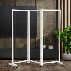 a white room divider in front of a wooden wall and potted plant on the floor