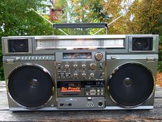 an old fashioned radio sitting on top of a wooden table in front of some trees