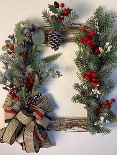 two christmas wreaths with pine cones, holly and berries hanging on a white wall