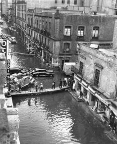 an old black and white photo of people walking on the side of a river in a city