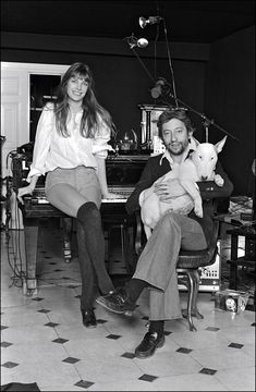 a man and woman sitting in front of a piano with a dog on their lap