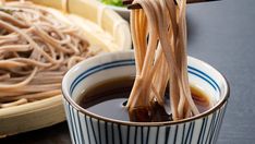 two chopsticks sticking out of a bowl of soup with noodles in the background