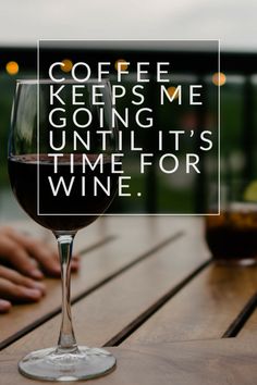 a glass of wine sitting on top of a wooden table next to a sign that says coffee keeps me going until it's time for wine