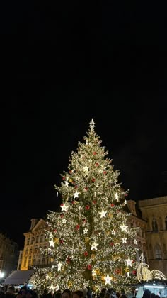 a large christmas tree is lit up in the middle of a city square at night