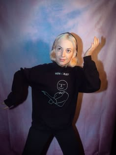 a woman with blonde hair wearing a black shirt and pants standing in front of a blue backdrop