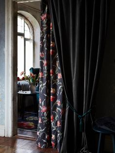 an open window with black curtains and flowers on the drapes in front of it