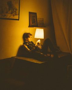 a young boy sitting on top of a couch under a lamp in a dark room