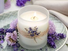 a white candle sitting on top of a plate next to purple flowers and lavenders