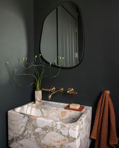 a bathroom sink with marble counter top and gold faucet in front of a round mirror