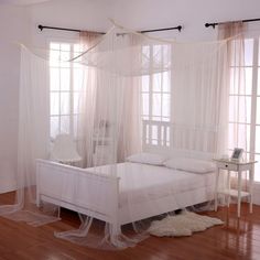 a white bed sitting in a bedroom on top of a hard wood floor next to two windows