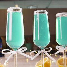 three champagne flutes with blue liquid and lemons in front of the glass are tied with a white ribbon