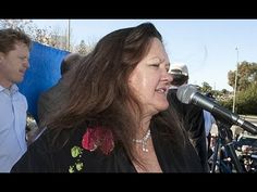 a woman singing into a microphone while standing next to a man in a blue shirt