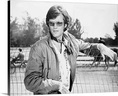 a man wearing sunglasses standing in front of a fence with his hand on the gate