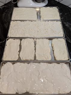 four pans filled with white frosting sitting on top of a counter next to a blender