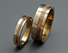 two wedding bands with wood inlays are shown on a gray surface, one is gold and the other is silver