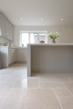 an empty kitchen with white cabinets and flowers on the counter top, in front of a window