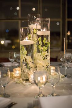 candles and flowers in glass vases on a table with silverware, wine glasses and napkins