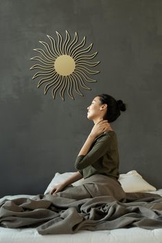 a woman sitting on top of a bed next to a sun wall hanging above her head