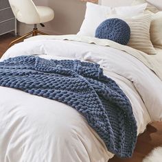 a bed with white sheets and blankets on top of it, next to a chair