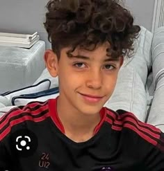 a young boy with curly hair sitting on a couch