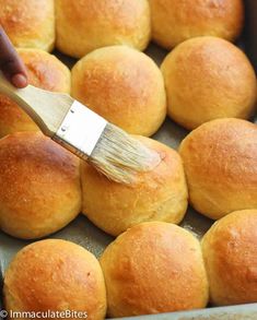 a person using a brush to paint the inside of rolls in a pan with butter