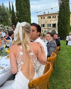 a bride and groom kissing in front of an outdoor dining area with people sitting at tables