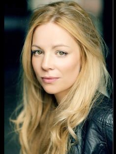 a woman with long blonde hair wearing a black leather jacket and looking at the camera