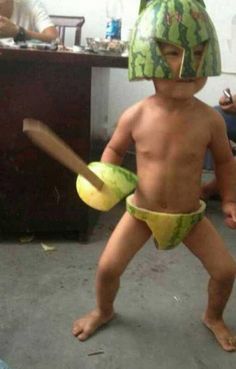 a young boy wearing a watermelon hat and holding a banana in his hand