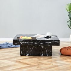 a marble coffee table sitting on top of a hard wood floor next to a potted plant