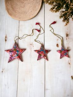 three red and pink stars hanging from string on white wooden planks next to a straw hat