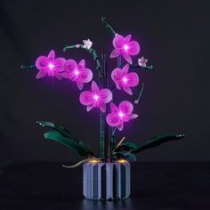 a purple flower arrangement in a black vase with pink flowers and green leaves on it