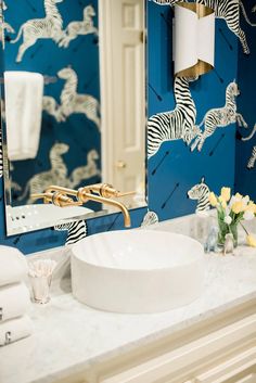 a bathroom sink with zebra wallpaper and gold faucets in the mirror above it