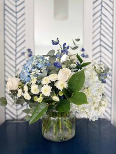 a vase filled with white and blue flowers on top of a table next to a mirror