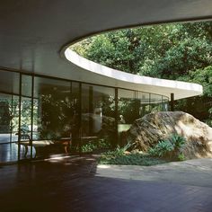 a large rock sitting in front of a glass walled entrance to a building surrounded by trees