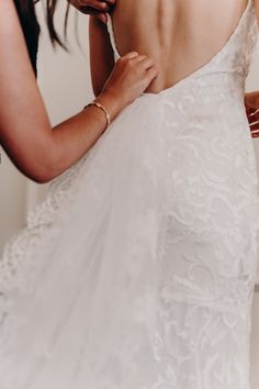 a woman in a wedding dress fixing the back of her dress