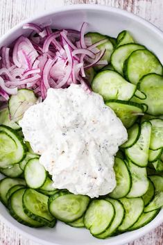 a bowl filled with cucumbers and onions next to sour cream sauce on top