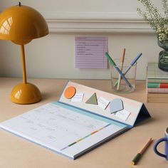 an open notebook on a desk next to a lamp and cup with pencils in it